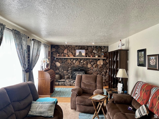 living area featuring a stone fireplace, a textured ceiling, and wood finished floors