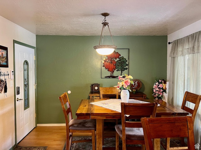 dining area featuring baseboards, a textured wall, a textured ceiling, and wood finished floors