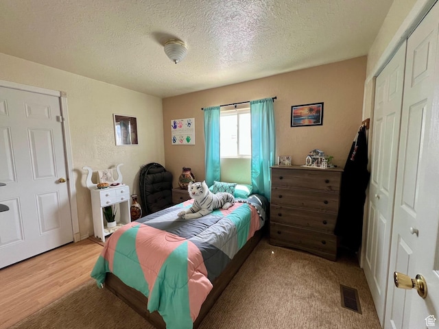 bedroom with a textured ceiling, a closet, light wood-type flooring, and visible vents