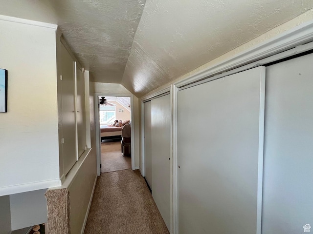 hall featuring vaulted ceiling, a textured ceiling, and carpet flooring