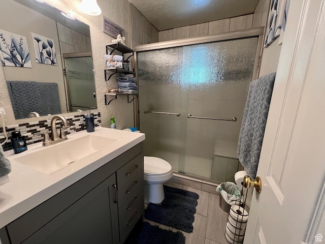 bathroom featuring toilet, tasteful backsplash, vanity, a textured wall, and a shower stall