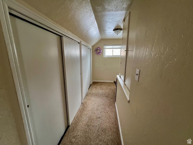 hallway with light colored carpet, a textured ceiling, vaulted ceiling, and a textured wall