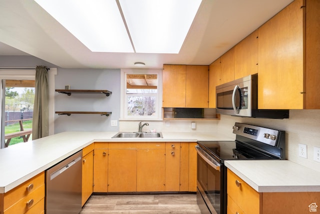 kitchen featuring a peninsula, light wood finished floors, a sink, open shelves, and stainless steel appliances