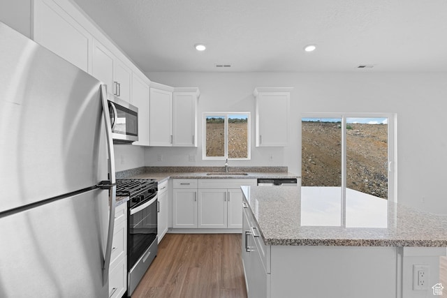 kitchen featuring a sink, a healthy amount of sunlight, light wood-style flooring, a center island, and appliances with stainless steel finishes