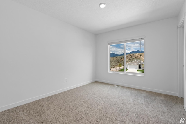 carpeted empty room featuring a mountain view and baseboards