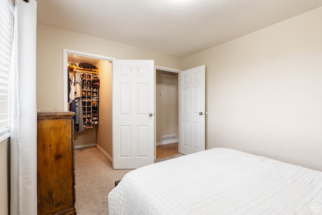 bedroom featuring a closet, light colored carpet, visible vents, a walk in closet, and baseboards
