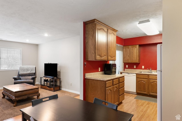 kitchen with a sink, brown cabinetry, white appliances, open floor plan, and light countertops