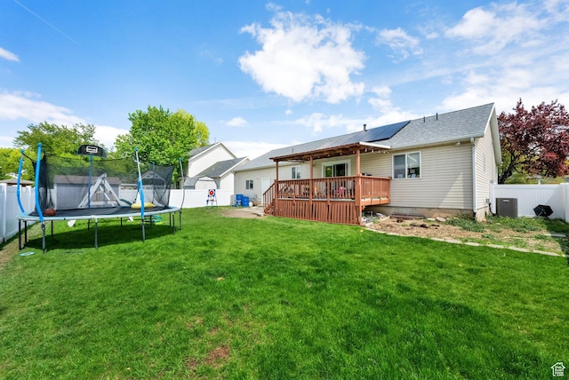 rear view of house with a trampoline, a deck, central AC unit, a fenced backyard, and a yard