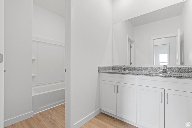 bathroom with double vanity, wood finished floors, baseboards, and a sink