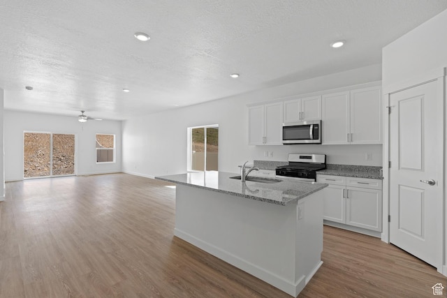 kitchen with white cabinetry, stainless steel appliances, light stone counters, and light wood-style flooring