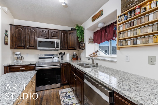 kitchen featuring a sink, stainless steel appliances, dark wood-type flooring, dark brown cabinetry, and light stone countertops