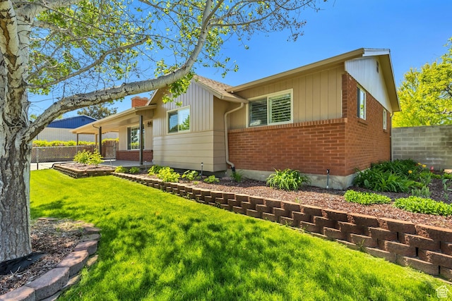 view of front facade with fence, board and batten siding, a front yard, brick siding, and a patio area