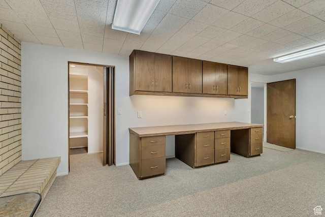 unfurnished office featuring baseboards, light carpet, and built in desk