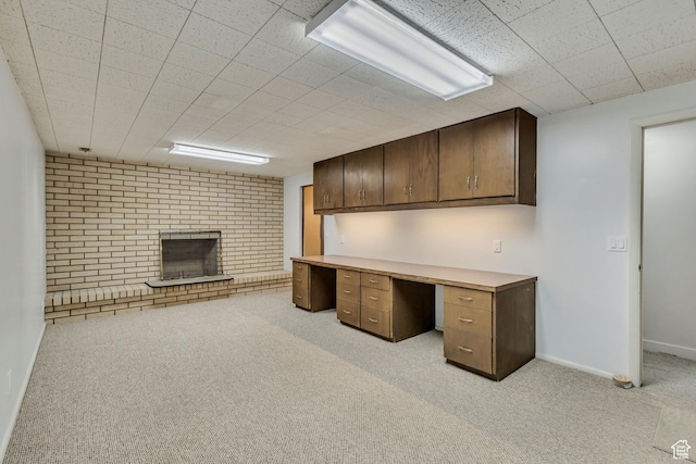unfurnished office with built in desk, light carpet, baseboards, and a brick fireplace