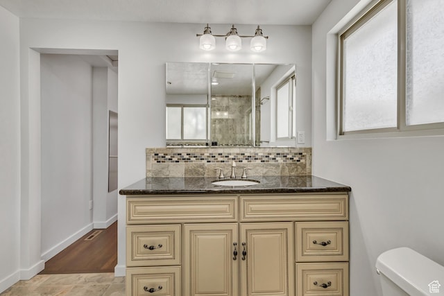 bathroom featuring toilet, vanity, backsplash, a shower stall, and baseboards