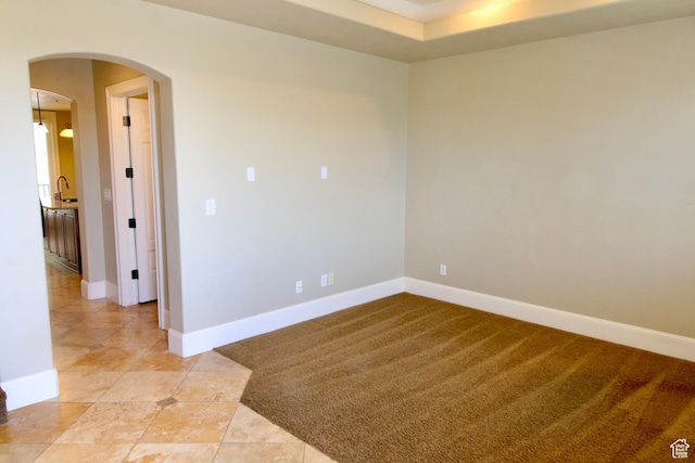 spare room featuring arched walkways, baseboards, light tile patterned floors, and light colored carpet