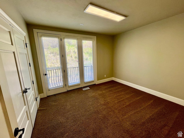 empty room featuring baseboards, dark carpet, and visible vents
