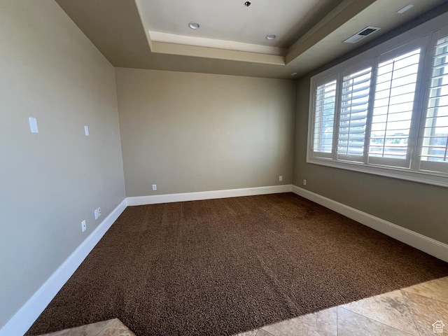 spare room featuring a tray ceiling, carpet floors, baseboards, and visible vents