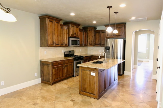 kitchen with a sink, stainless steel appliances, light stone counters, backsplash, and arched walkways