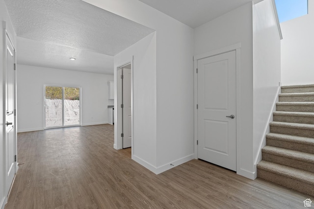 interior space featuring a textured ceiling, wood finished floors, baseboards, and stairs