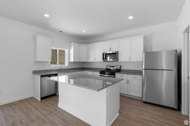 kitchen with a sink, stainless steel appliances, light stone counters, white cabinetry, and a center island