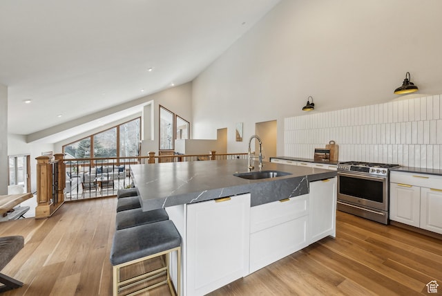 kitchen featuring high vaulted ceiling, a sink, dark countertops, stainless steel range with gas stovetop, and white cabinetry