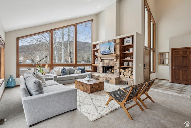 carpeted living room featuring a high ceiling, baseboards, and a stone fireplace
