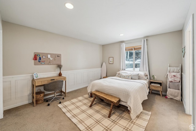 bedroom featuring wainscoting, light colored carpet, a decorative wall, and recessed lighting