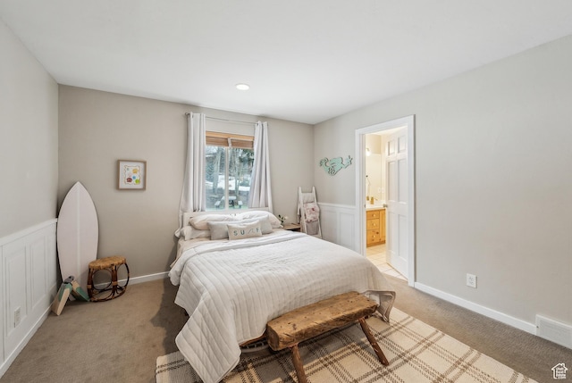 bedroom with wainscoting, light colored carpet, connected bathroom, and visible vents