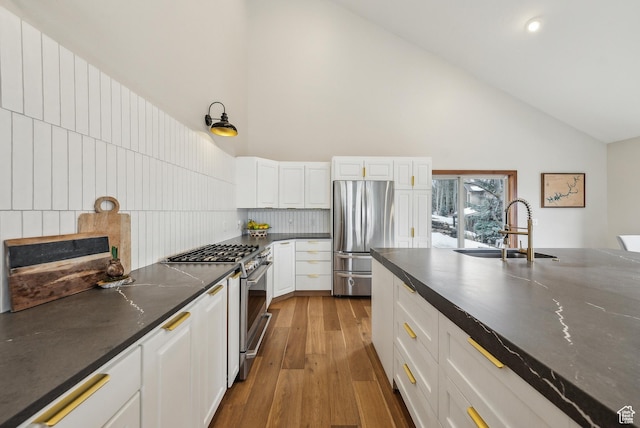 kitchen with light wood-style flooring, a sink, high vaulted ceiling, dark countertops, and stainless steel appliances