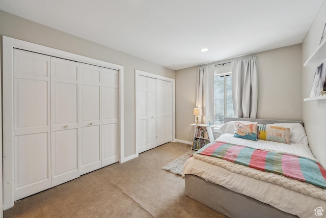 bedroom featuring baseboards, recessed lighting, light carpet, and two closets