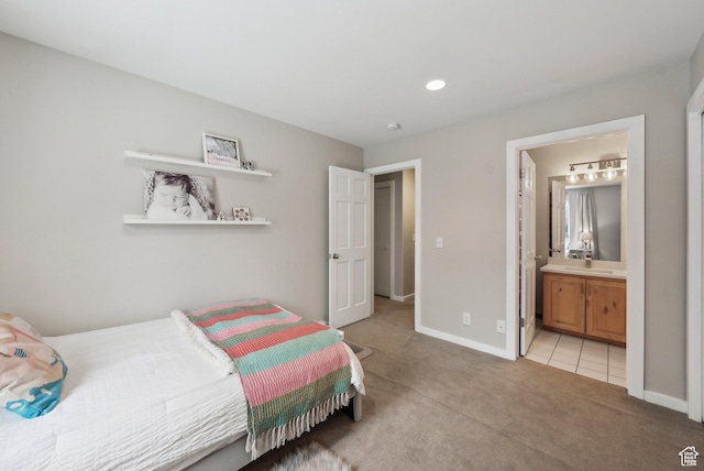 bedroom featuring light tile patterned floors, a sink, ensuite bathroom, baseboards, and light colored carpet