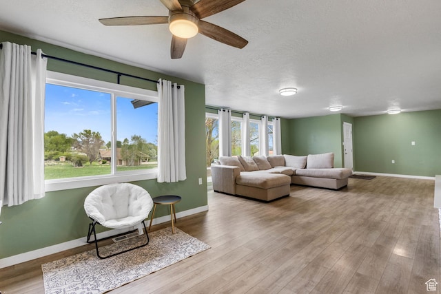 living room featuring baseboards, ceiling fan, a textured ceiling, and wood finished floors