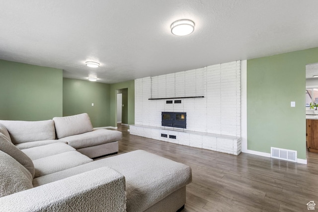 living area with a fireplace, baseboards, visible vents, and wood finished floors