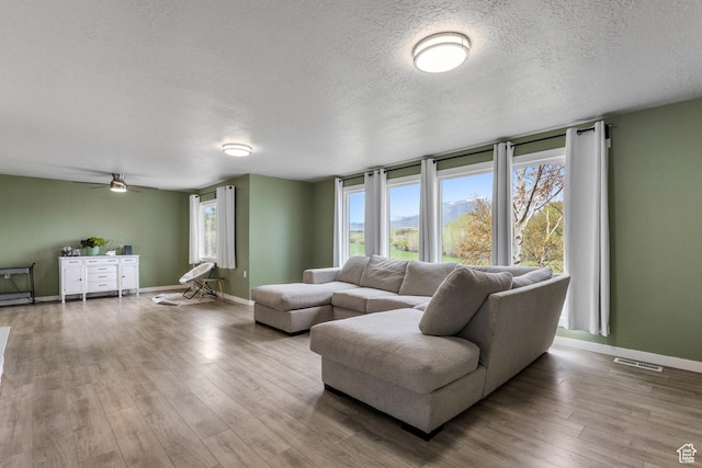 living area featuring a textured ceiling, baseboards, a ceiling fan, and visible vents