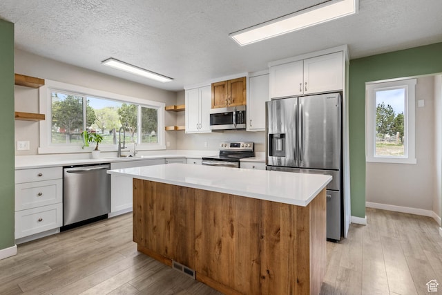 kitchen featuring light wood-style floors, stainless steel appliances, open shelves, and a sink