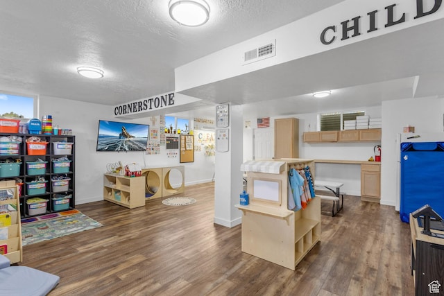 interior space with a textured ceiling, visible vents, wood finished floors, and baseboards