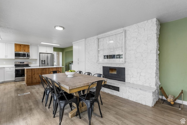 dining room with a stone fireplace, light wood-type flooring, and a textured ceiling