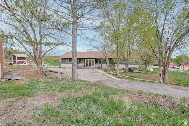 ranch-style house featuring covered porch, dirt driveway, an outdoor structure, and a storage shed