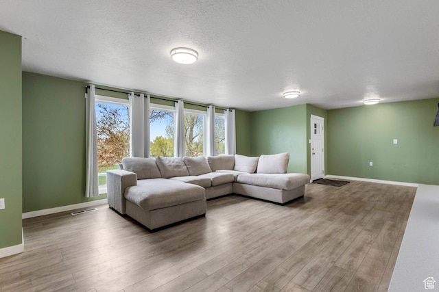 living room featuring a textured ceiling, baseboards, visible vents, and wood finished floors