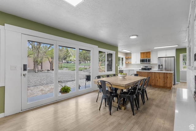 dining space with baseboards, light wood finished floors, a textured ceiling, and plenty of natural light