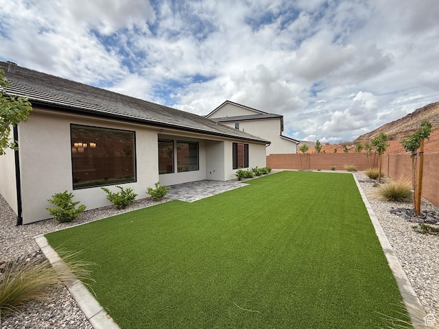 back of house with a lawn, stucco siding, a fenced backyard, and a patio