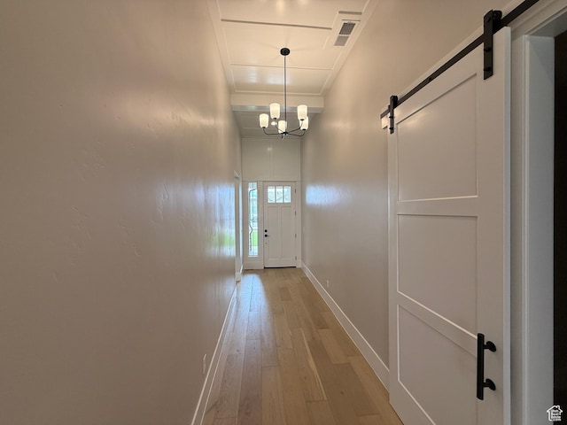 doorway to outside featuring a barn door, visible vents, light wood finished floors, a chandelier, and baseboards