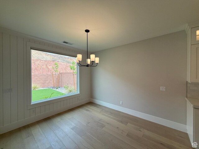 unfurnished dining area with baseboards, light wood-style floors, a chandelier, and visible vents
