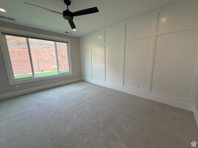 spare room featuring ceiling fan, a decorative wall, visible vents, and light colored carpet