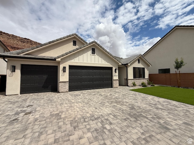 view of front facade featuring stone siding, a garage, stucco siding, fence, and driveway