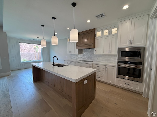 kitchen featuring visible vents, a sink, custom range hood, stainless steel appliances, and an island with sink