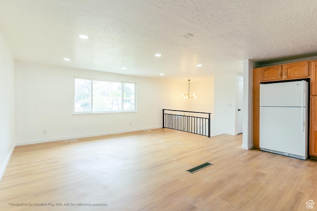 unfurnished room with light wood finished floors, a chandelier, visible vents, and a textured ceiling