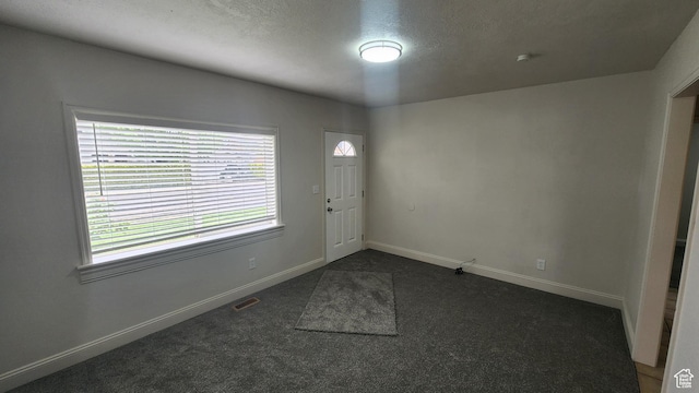 foyer with baseboards, dark carpet, visible vents, and a textured ceiling