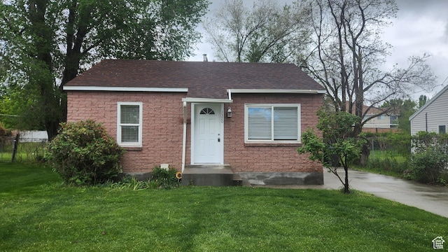 view of front of home featuring roof with shingles, fence, and a front lawn